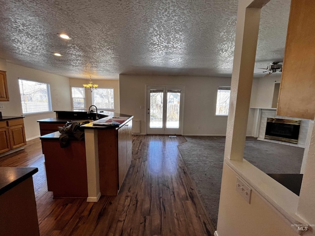 kitchen with dark wood finished floors, dark countertops, an island with sink, brown cabinets, and a fireplace