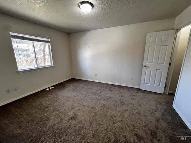 empty room featuring a textured ceiling, dark colored carpet, visible vents, and baseboards