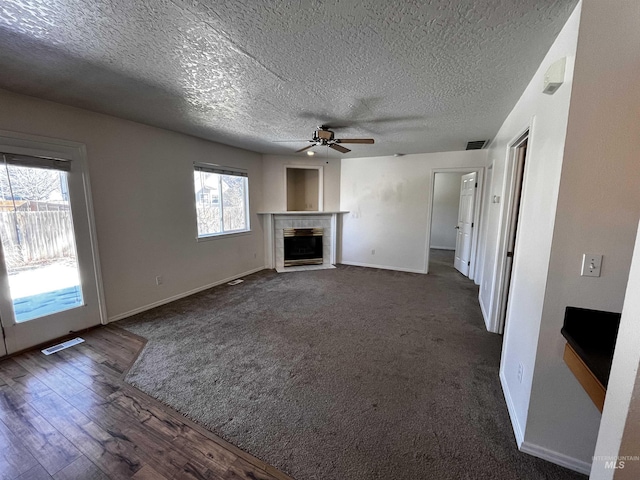 unfurnished living room with a ceiling fan, a tile fireplace, dark wood-style flooring, and visible vents