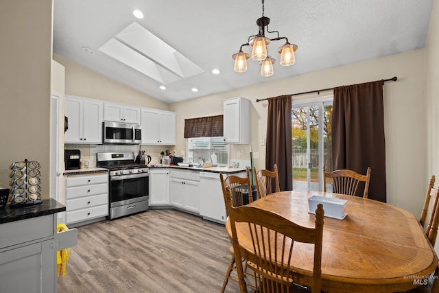 kitchen featuring appliances with stainless steel finishes, white cabinetry, vaulted ceiling with skylight, pendant lighting, and light hardwood / wood-style flooring