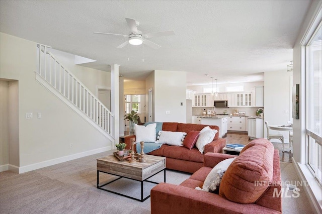 living room with baseboards, a ceiling fan, stairs, and a textured ceiling