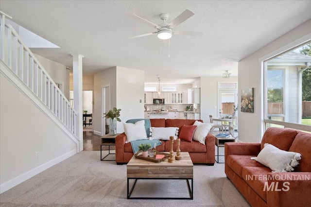 living room with light colored carpet, a textured ceiling, stairs, and ceiling fan