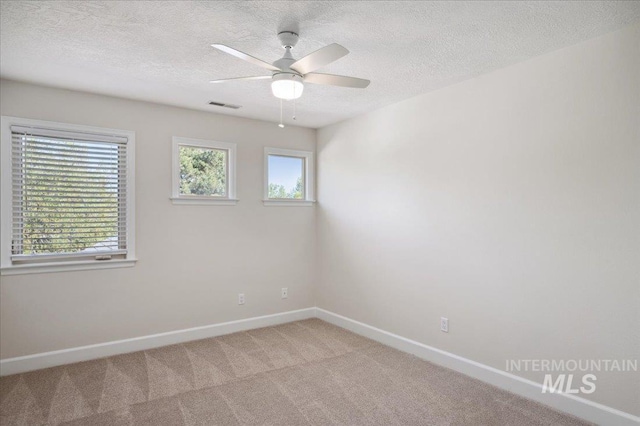 carpeted spare room featuring baseboards, ceiling fan, a textured ceiling, and visible vents