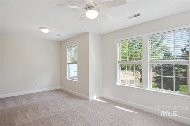 spare room featuring visible vents, a ceiling fan, baseboards, and light carpet