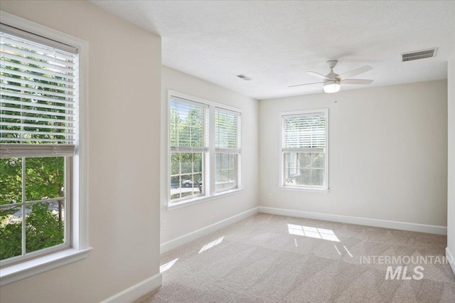 carpeted empty room featuring a healthy amount of sunlight, baseboards, and visible vents