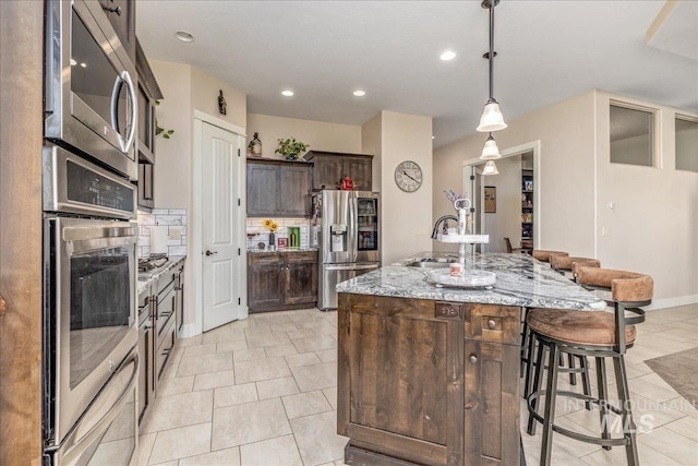 4595 N Tirso Ave, Meridian, ID 83646 - kitchen with dark brown cabinetry, a kitchen bar, appliances with stainless steel finishes, a center island with sink, and a sink