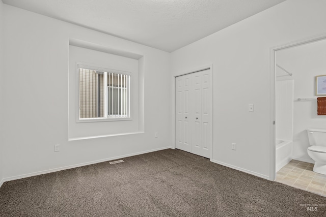 unfurnished bedroom with a closet, ensuite bathroom, carpet, and a textured ceiling