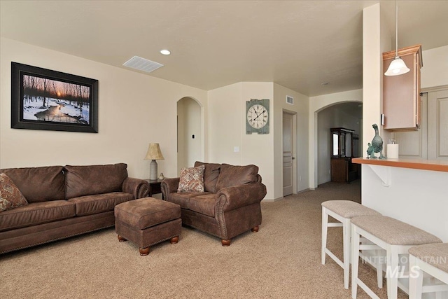 living area with arched walkways, visible vents, light colored carpet, and recessed lighting