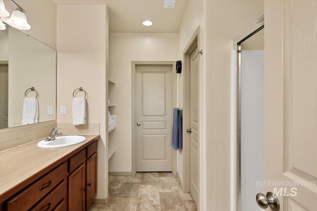 full bath featuring tiled shower, vanity, and baseboards