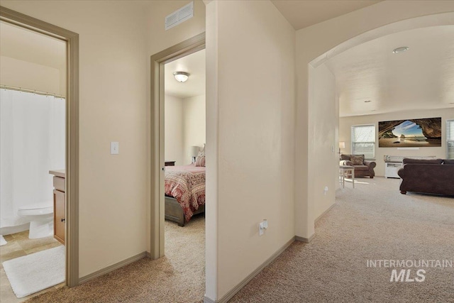 hallway featuring visible vents, arched walkways, light colored carpet, and baseboards