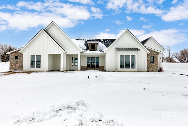 snow covered back of property with a standing seam roof, stone siding, and board and batten siding