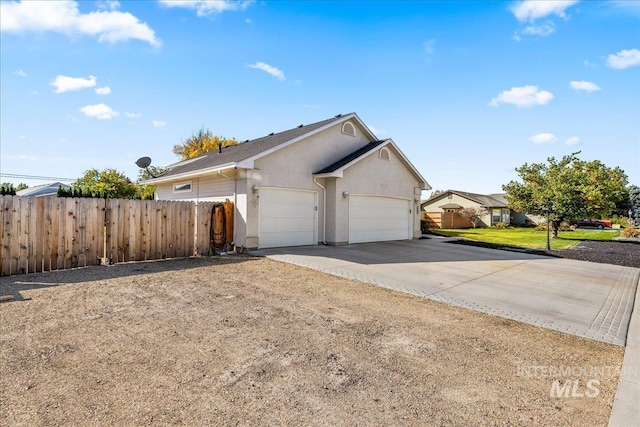 view of side of property with concrete driveway, fence, an attached garage, and stucco siding