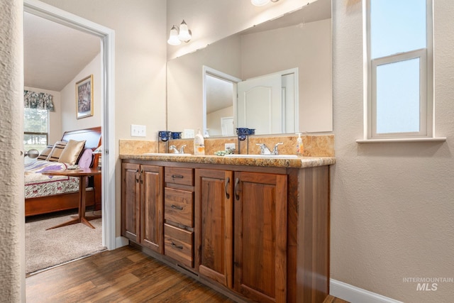 ensuite bathroom with connected bathroom, baseboards, double vanity, wood finished floors, and a sink