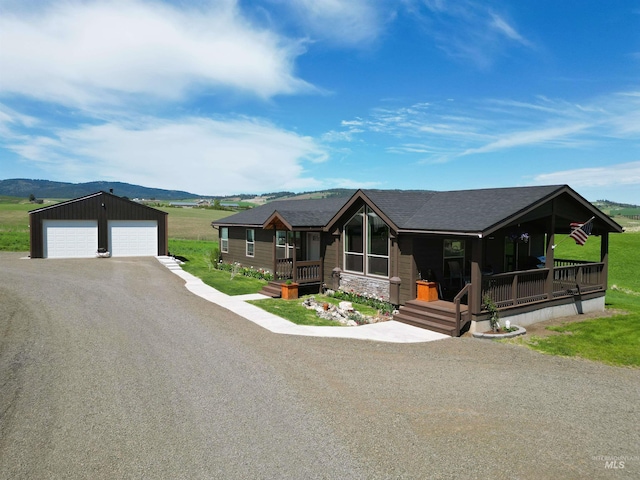 view of front of property featuring a shingled roof, a porch, a garage, an outdoor structure, and stone siding