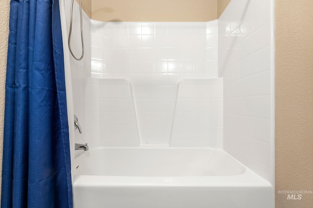 bathroom with a textured wall and shower / bath combination with curtain