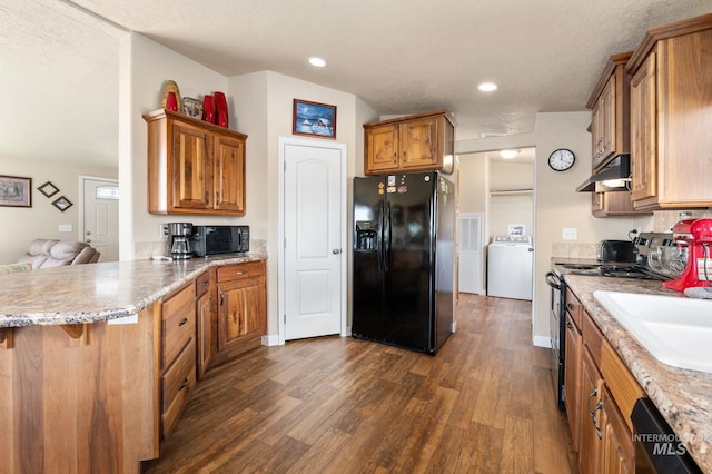 kitchen with dark wood-style floors, a peninsula, washer / clothes dryer, black appliances, and under cabinet range hood