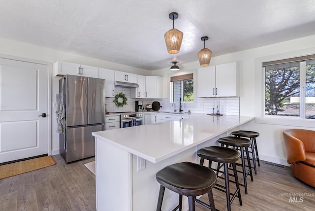 kitchen featuring stainless steel appliances, a peninsula, under cabinet range hood, and wood finished floors