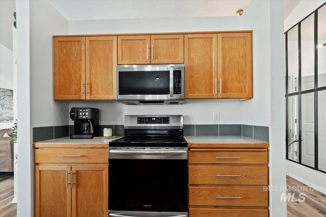 kitchen featuring stainless steel appliances, brown cabinets, wood finished floors, and light countertops