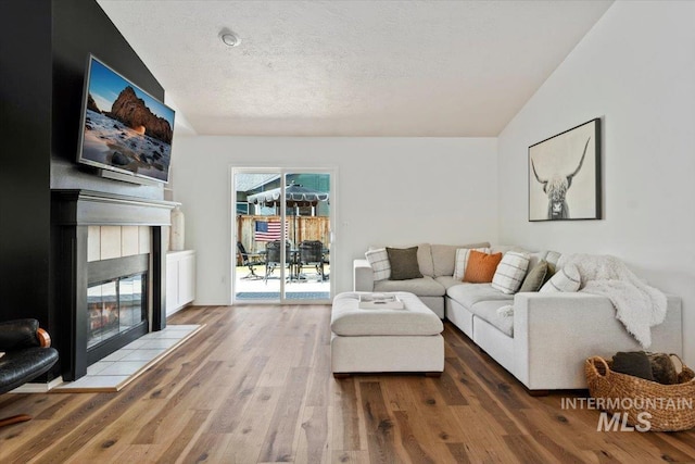 living room with a tiled fireplace, lofted ceiling, wood finished floors, and a textured ceiling