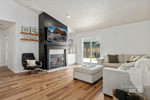 living area featuring baseboards, a fireplace, wood finished floors, a textured ceiling, and high vaulted ceiling