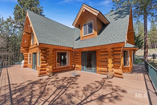 back of house featuring a shingled roof, a wooden deck, and log exterior