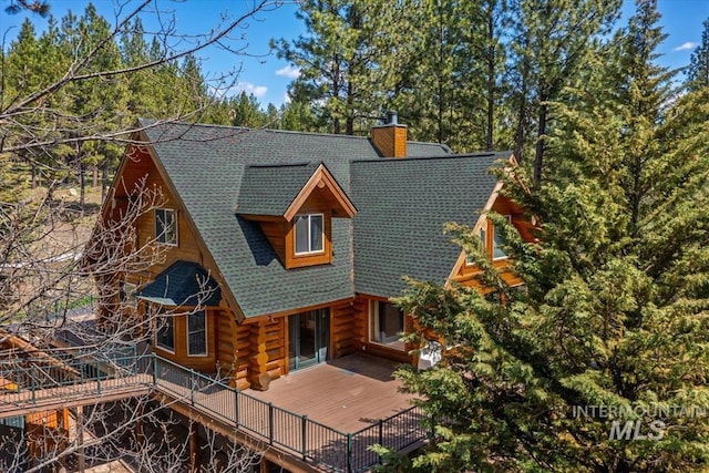 back of property featuring a deck, log siding, a shingled roof, and a chimney
