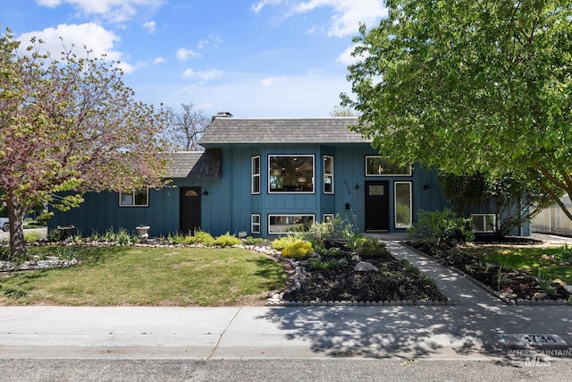 view of front of home with roof with shingles, a front yard, and board and batten siding
