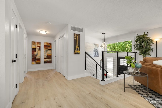 hall with an upstairs landing, light wood-style floors, baseboards, and a textured ceiling