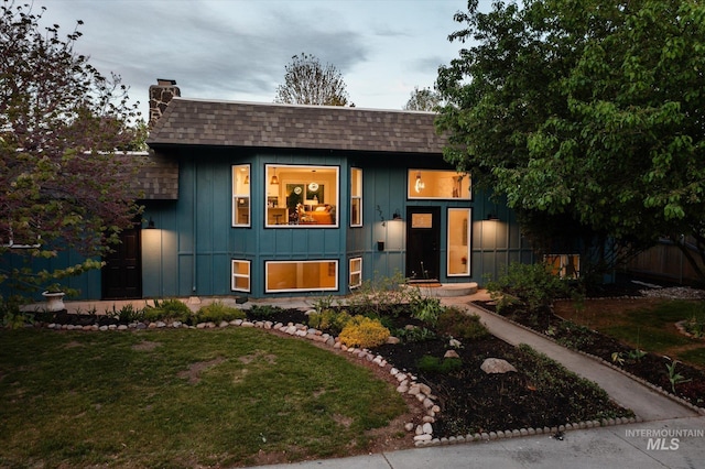 view of front of home featuring a chimney, roof with shingles, board and batten siding, and a front yard