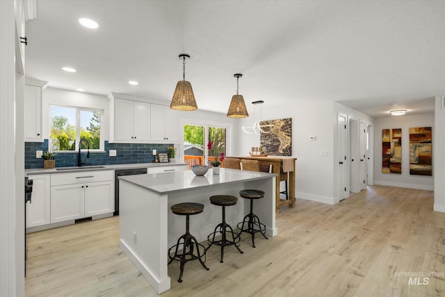 kitchen featuring a sink, dishwashing machine, a kitchen breakfast bar, decorative backsplash, and light wood-style floors