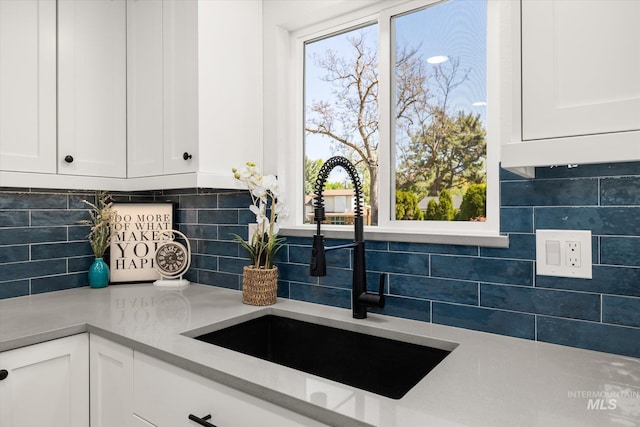kitchen view of a sink, white cabinets, backsplash, and light countertops