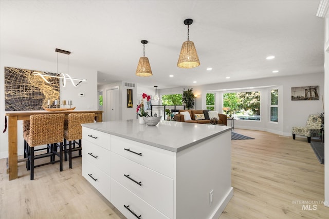kitchen featuring light wood finished floors, a center island, recessed lighting, white cabinetry, and pendant lighting