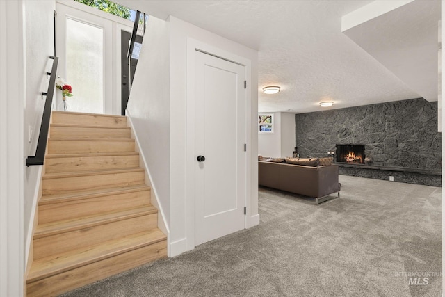 staircase featuring a textured ceiling, carpet, and a stone fireplace