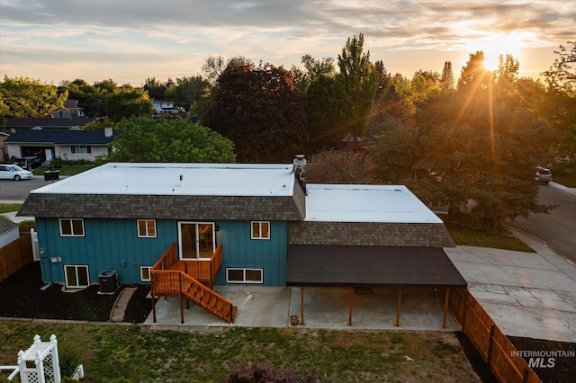 back of property at dusk with central AC, stairs, a shingled roof, and a chimney