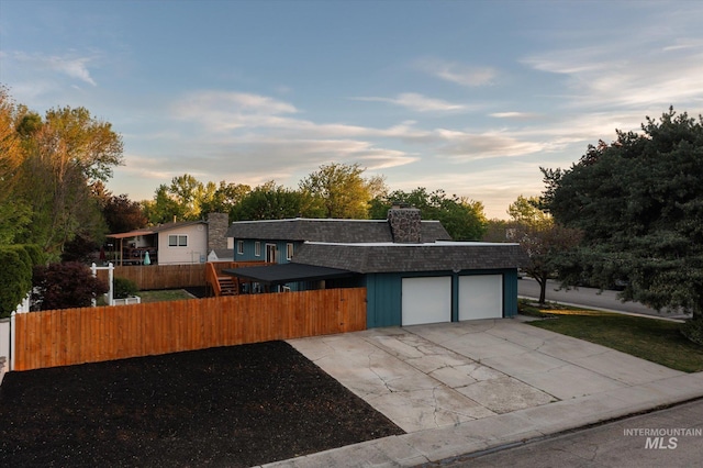 view of front of home featuring an attached garage, a shingled roof, driveway, fence, and a chimney