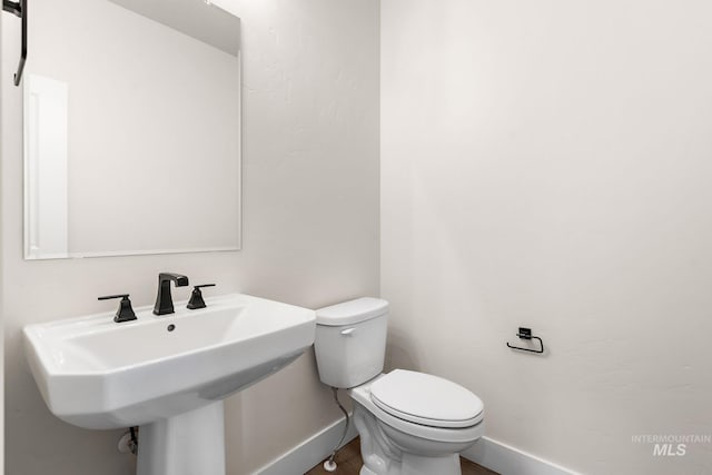 bathroom featuring toilet, wood finished floors, baseboards, and a sink