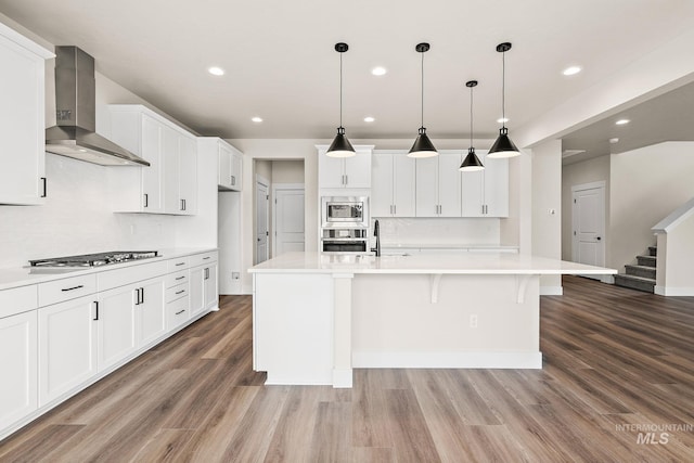 kitchen with light countertops, wall chimney range hood, white cabinets, and appliances with stainless steel finishes