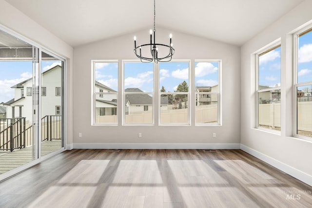 unfurnished dining area featuring vaulted ceiling, a notable chandelier, wood finished floors, and a wealth of natural light