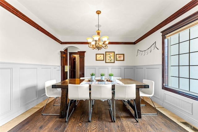 dining area featuring a decorative wall, ornamental molding, an inviting chandelier, and wood finished floors