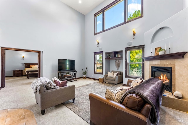 carpeted living area featuring visible vents, baseboards, a high ceiling, and a tiled fireplace