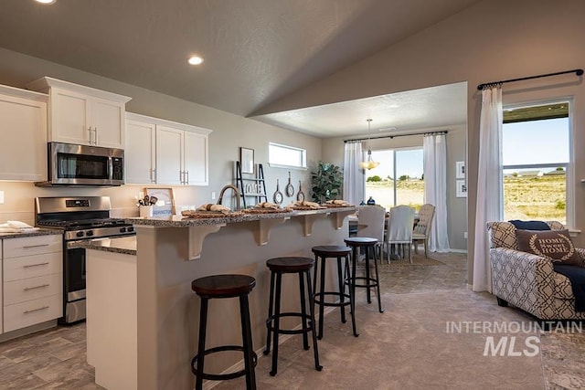 kitchen featuring a kitchen island with sink, a breakfast bar, vaulted ceiling, white cabinets, and appliances with stainless steel finishes
