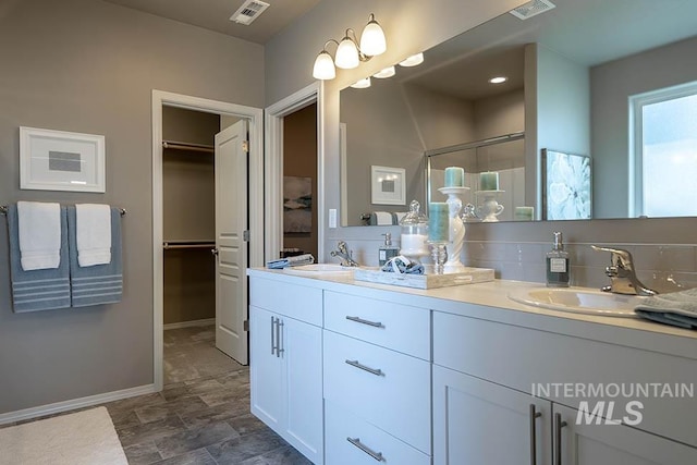 bathroom with double vanity, a sink, baseboards, visible vents, and a stall shower