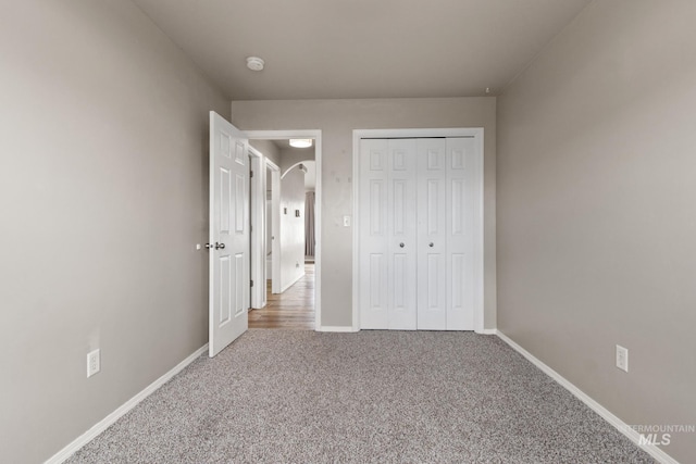 unfurnished bedroom featuring carpet, baseboards, a closet, and arched walkways