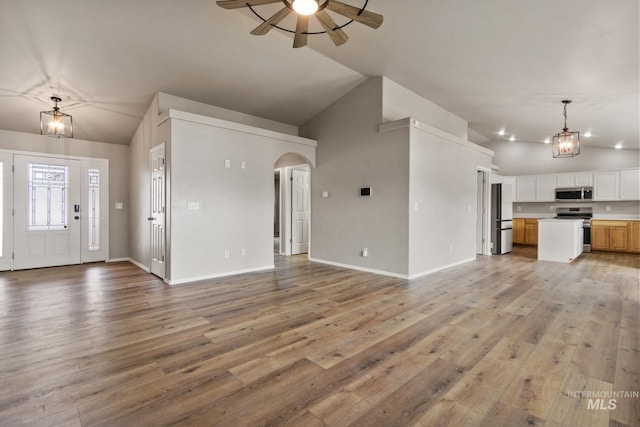 unfurnished living room featuring light wood-style floors, ceiling fan with notable chandelier, high vaulted ceiling, arched walkways, and baseboards