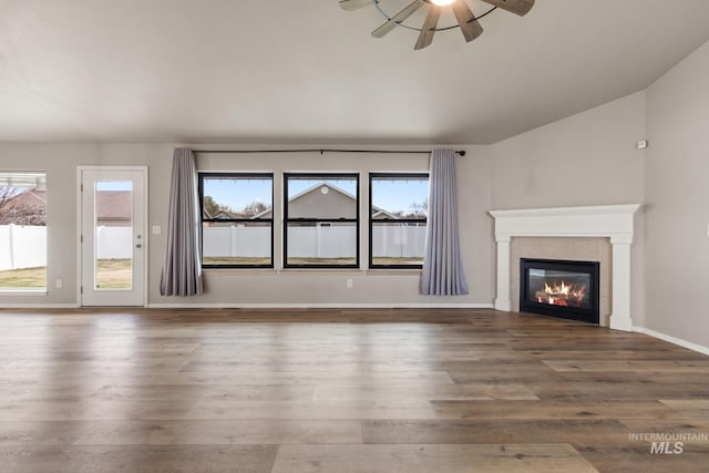 unfurnished living room with baseboards, a tiled fireplace, ceiling fan, vaulted ceiling, and wood finished floors