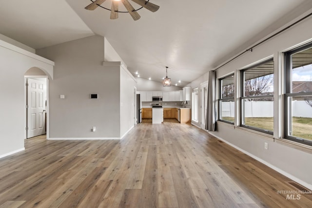 unfurnished living room with light wood-style floors, ceiling fan, arched walkways, lofted ceiling, and baseboards