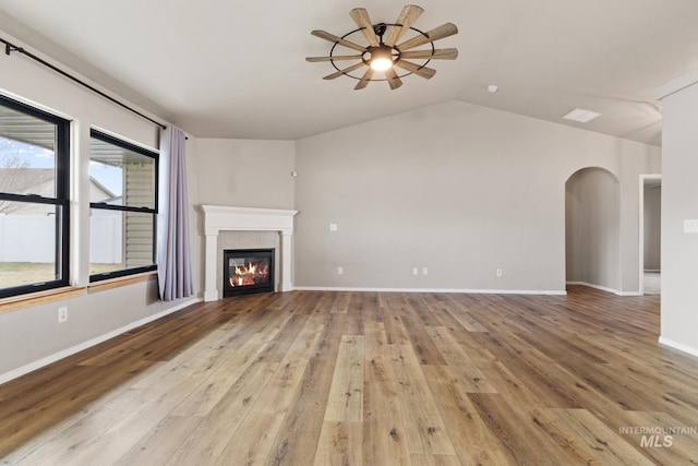 unfurnished living room with arched walkways, a ceiling fan, a tiled fireplace, lofted ceiling, and hardwood / wood-style flooring