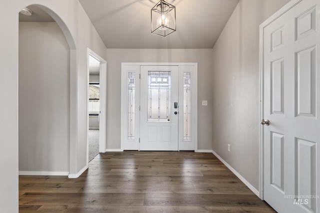 entrance foyer with a chandelier, arched walkways, dark wood-type flooring, and baseboards