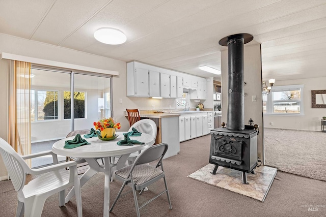 kitchen featuring light carpet, kitchen peninsula, white cabinets, and a wood stove