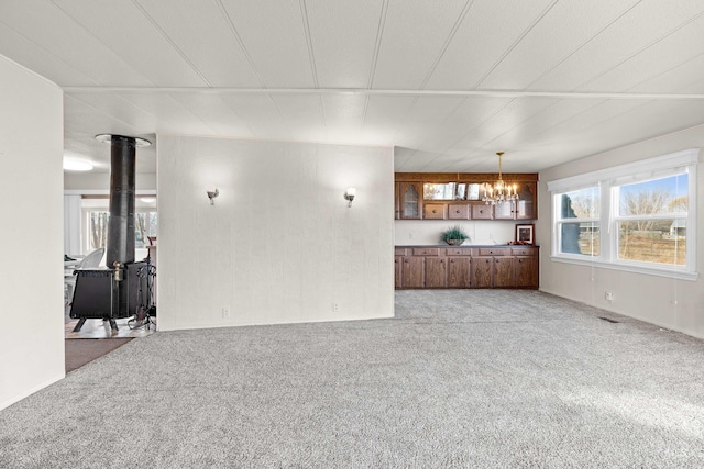 unfurnished living room featuring a notable chandelier, light colored carpet, and a wood stove